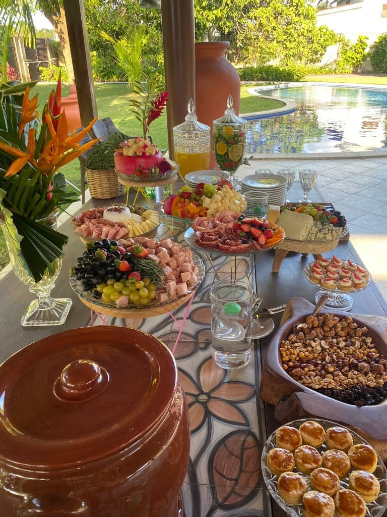 Mesa de petiscos com frios, frutas e salgados à beira da piscina
